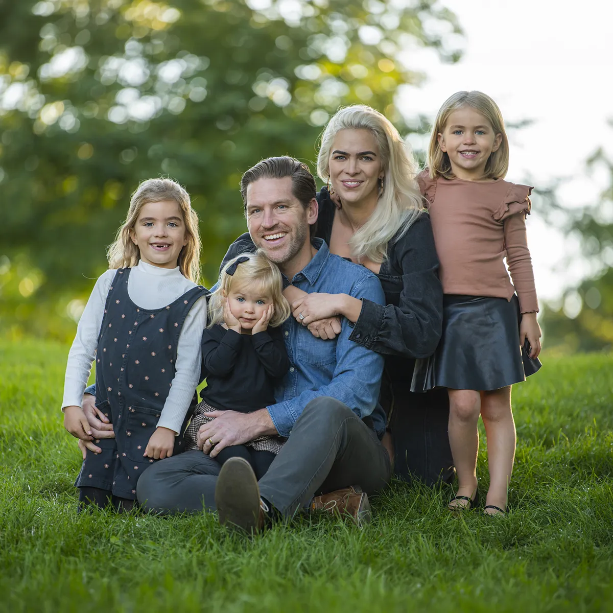 Parents and their three children posing together on the grass beneath leafy trees