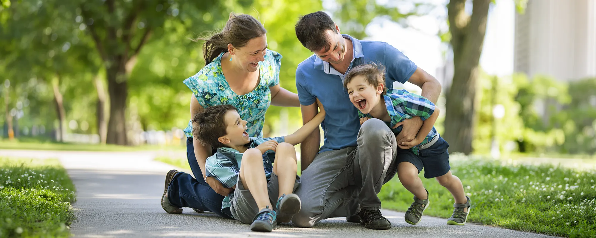 Parents and their two children laughing together on a leafy park path