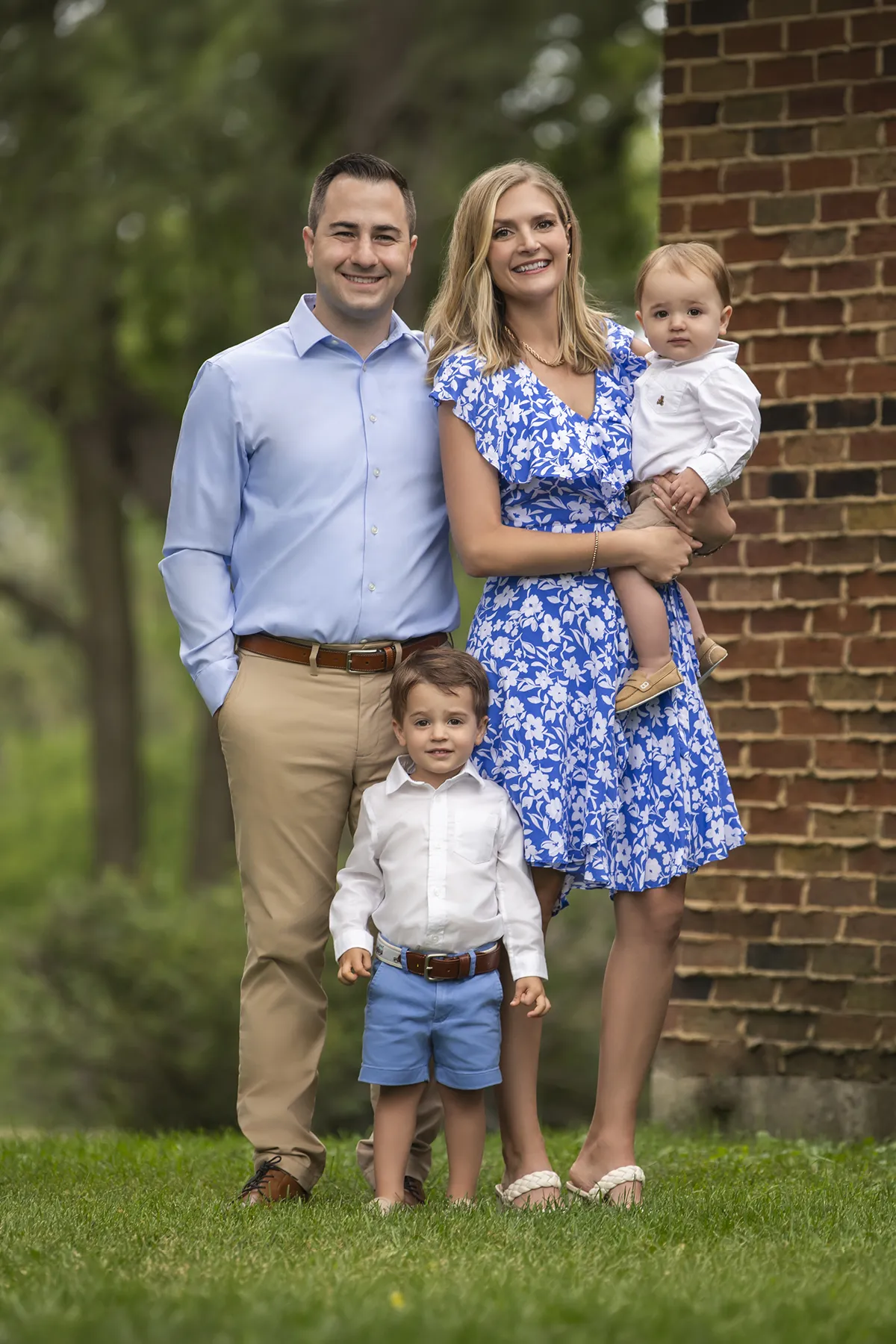 Parents with their two young children standing on grass beside a brick wall